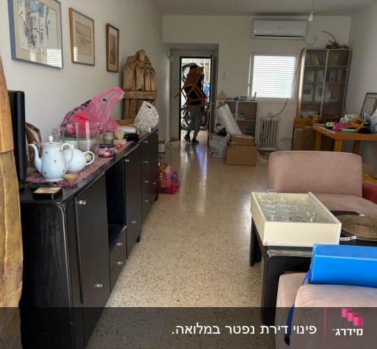 חדר עם רהיטים, קופסאות וכלי מטבח על מדף